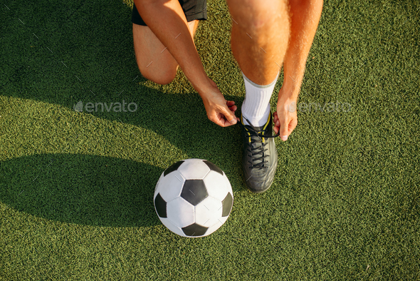 Male soccer player ties his shoelaces on boots