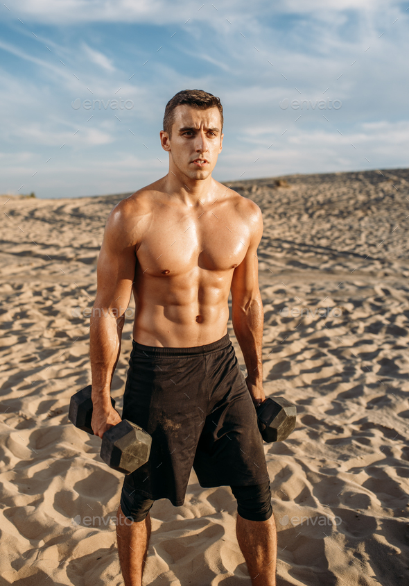 Muscular male athlete with dumbbells in desert