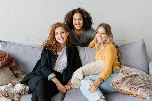 Group of friendly intercultural girls in smart casual sitting on sofa