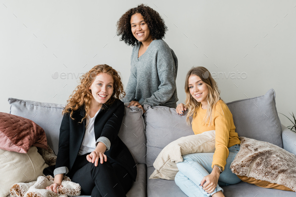Group of cheerful friendly girls relaxing on soft comfortable sofa