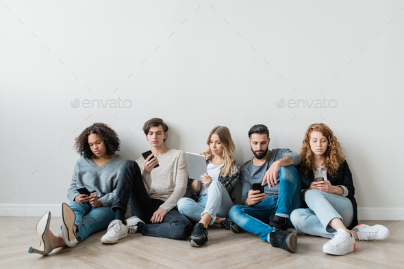 Group of serious millennials with smartphones and touchpad scrolling in gadgets