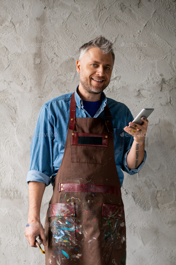 Happy and successful painter with smartphone and paintbrush
