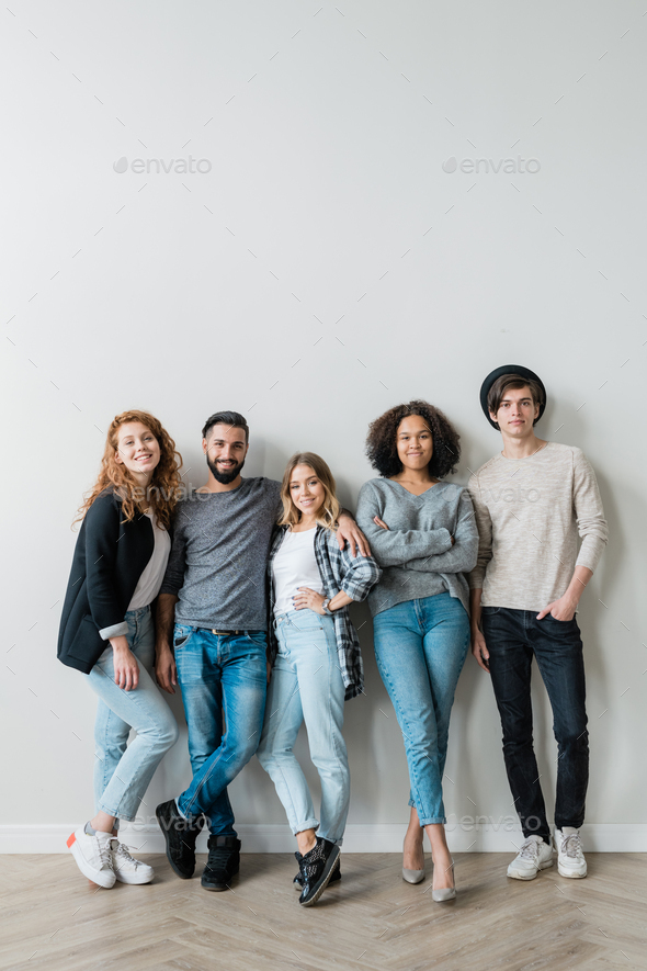 Group of cheerful young affectionate friends in jeans and pullovers