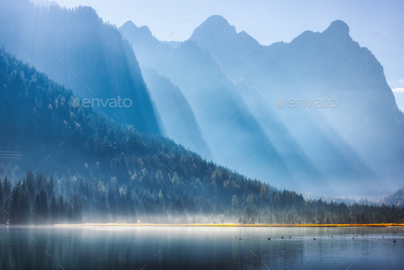 Majestic mountains in bright sunbeams and foggy lake at sunrise - Stock Photo - Images