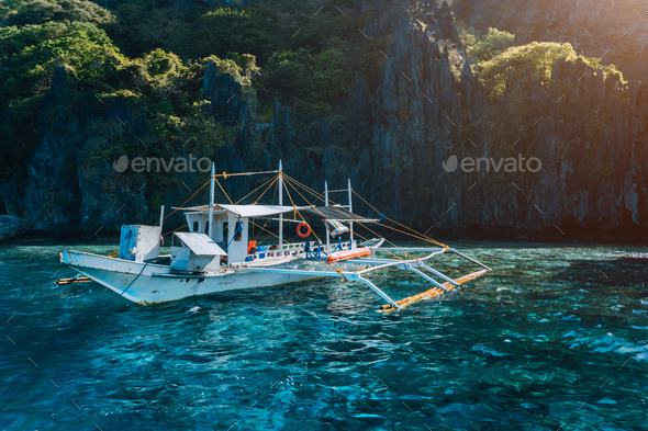 Banca local boat on turquoise water against huge limestone cliffs. Island hopping tour trip - Stock Photo - Images