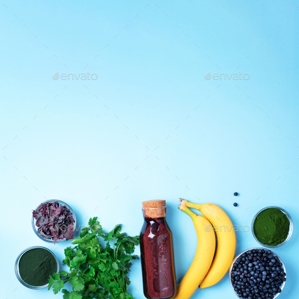 Blueberries, bilberry, barley grass, spirulina, orange juice, dulse, cilantro on blue background - Stock Photo - Images