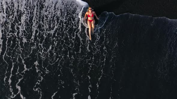 Top View of a Woman in a Red Swimsuit Lying on a Black Beach on the Surf Line. Coast of the Island alt