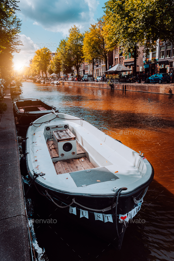 Channel in Amsterdam at autumn sunset. Boat in front of tree-lined canal, white clouds in the sky