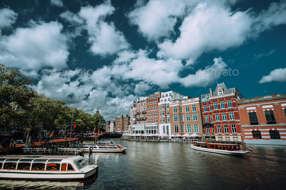 Classical Amsterdam cityscape. Cruise boats floating on the channel, river side promenade, cafes