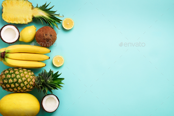 Fresh organic yellow fruits over blue background. Monochrome concept with banana, coconut, pineapple - Stock Photo - Images