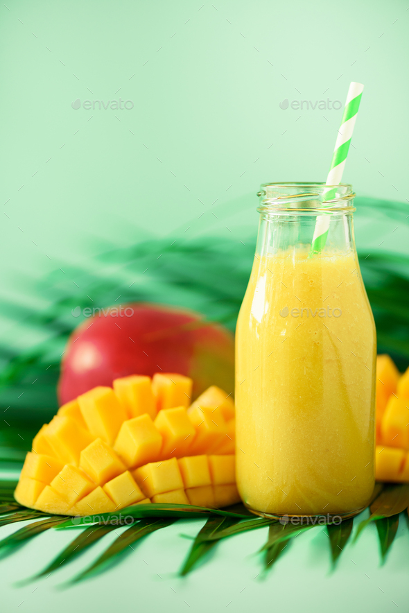 Delicious juicy smoothie with orange fruit and mango on turquoise background. Copy space. Pop art - Stock Photo - Images