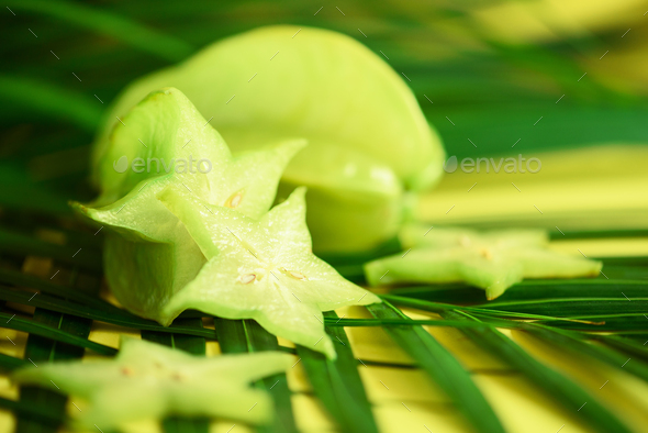 Exotic star fruit or averrhoa carambola over tropical green palm leaves on yellow background. Copy - Stock Photo - Images