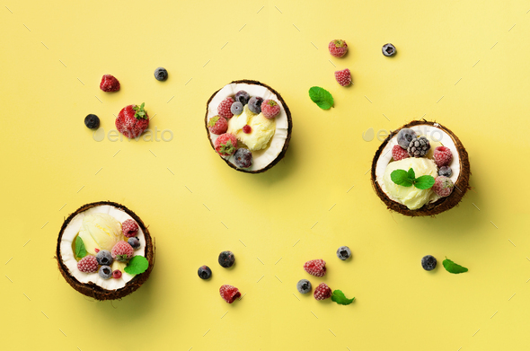 Coconut ice cream with fresh berries in coconuts halves on yellow background with copy space. Top - Stock Photo - Images