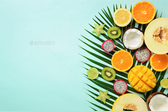 Exotic fruits and tropical palm leaves on pastel turquoise background - papaya, mango, pineapple