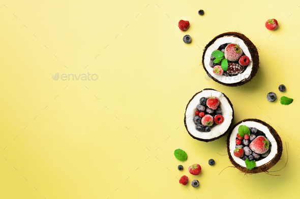 Fresh organic berries, mint leaves inside ripe coconuts on yellow background with copy space. Top - Stock Photo - Images