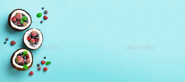 Fresh organic berries, mint leaves inside ripe coconuts on blue background with copy space. Top View - Stock Photo - Images