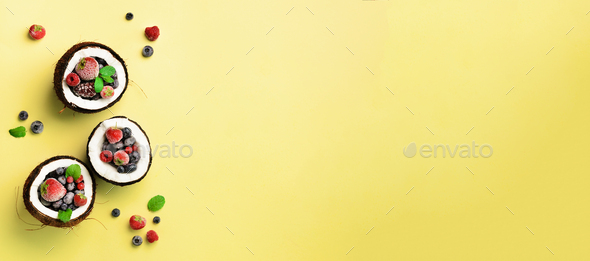 Fresh organic berries, mint leaves inside ripe coconuts on yellow background with copy space. Top - Stock Photo - Images