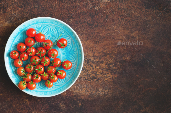 Many fresh cherry tomatoes in blue plate on brown background. Free space for your text