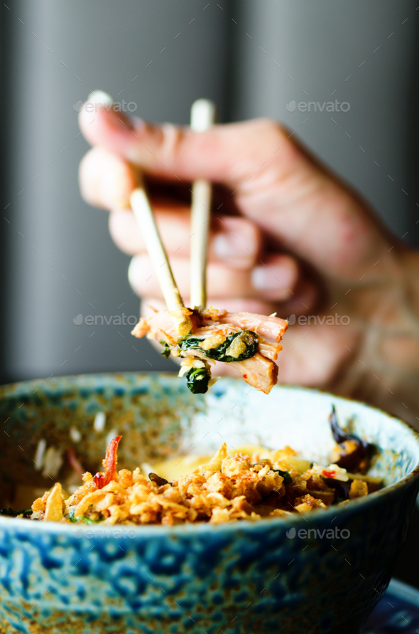 Man's hand holding chopsticks over a plate of Japanese, thai, chinese meal - rice, mushroom - Stock Photo - Images