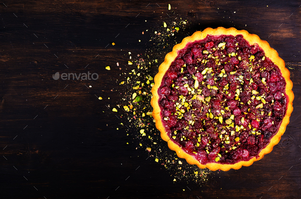 Sweet tart with raspberries, cherries, red currants with pistachios, powdered sugar on dark wooden - Stock Photo - Images