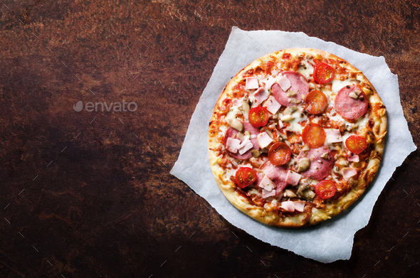 Fresh italian pizza with mushrooms, ham, tomatoes, cheese on on backing paper, dark background. Copy - Stock Photo - Images