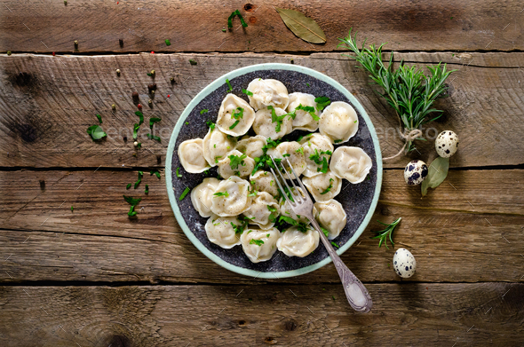 Traditional russian pelmeni, ravioli, dumplings with meat on wooden table with flour, parsley, quail - Stock Photo - Images