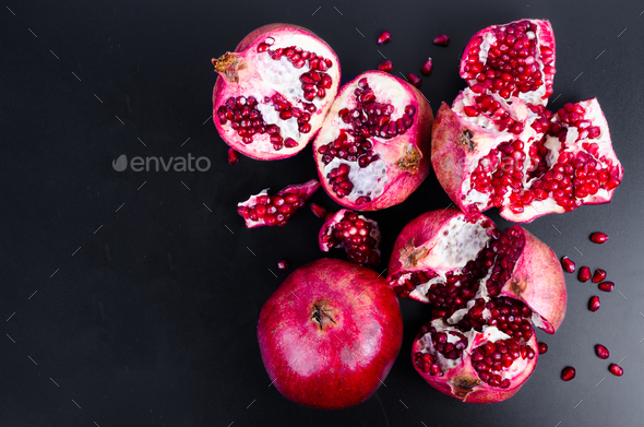Ripe juice pomegranate fruit on black background - whole and cut, top view