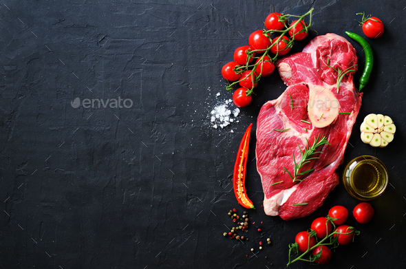 Raw meat steaks with cherry tomatoes, hot pepper, garlic, oil and herbs on dark stone, concrete - Stock Photo - Images