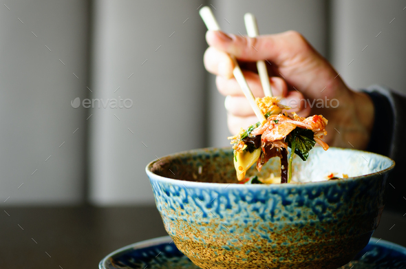 Man's hand holding chopsticks over a plate of Japanese, thai, chinese meal - rice, mushroom - Stock Photo - Images