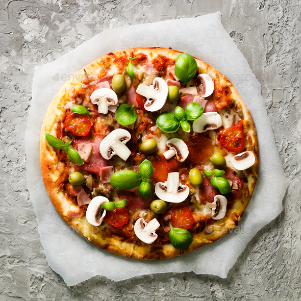 Fresh italian pizza with mushrooms, ham, tomatoes, cheese on on backing paper, grey concrete - Stock Photo - Images