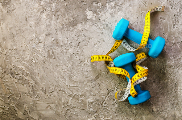 Fitness concept. Turquoise dumbbells and yellow measuring tape. Copyspace
