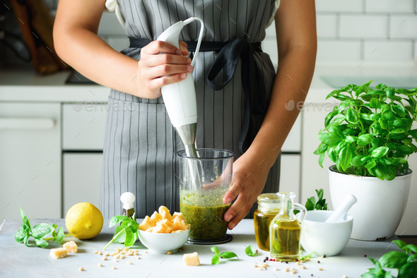 Woman using hand blender to make pesto. White kitchen interior design. Copy space. Vegetarian, clean - Stock Photo - Images