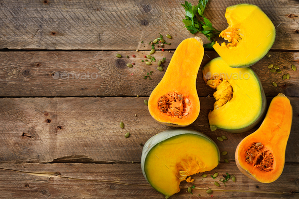 Cut ripe orange pumpkin with seeds and herbs on rustic wooden background. Vegetarian and raw organic - Stock Photo - Images