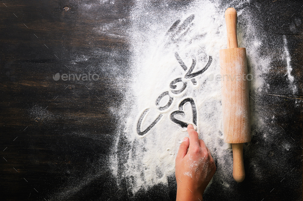 Baking background. Heart of flour, text Cook and rolling pin on dark table with copy space, top view