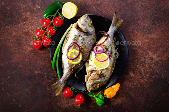 Cooked baked grilled fish, dorado, sea bream with lemon, herbs, vegetables and spices on rustic - Stock Photo - Images