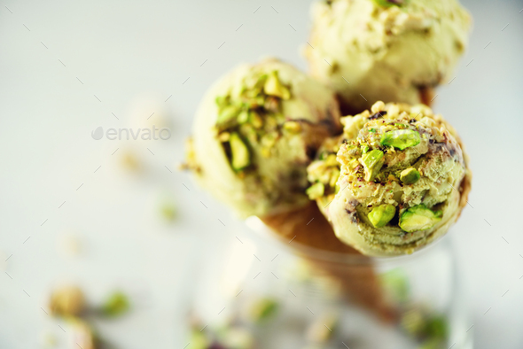 Green ice cream in waffle cone with chocolate and pistachio nuts on grey stone background. Summer - Stock Photo - Images