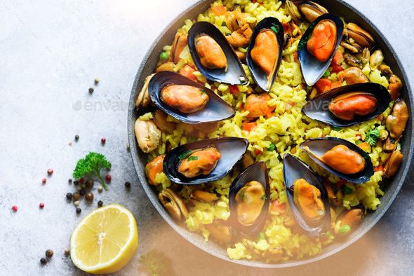 Traditional spanish seafood paella in pan rice, peas, shrimps, mussels, squid on light grey concrete - Stock Photo - Images