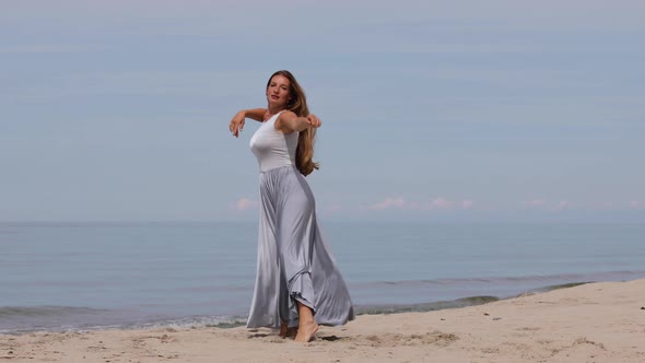 Beautiful Young Woman in a Long Dress Dancing on The Beach 
