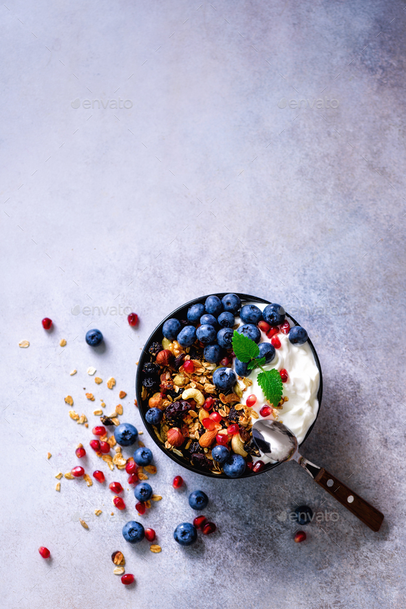 Tasty homemade granola, yogurt, fresh organic berries, pomegranate, mint on grey concrete background - Stock Photo - Images