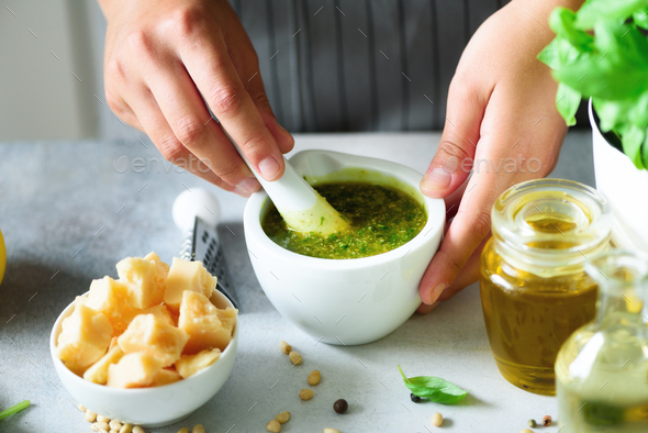 Woman hands making italian pesto in bowl. Ingredients - basil, lemon, parmesan, pine nuts, garlic - Stock Photo - Images