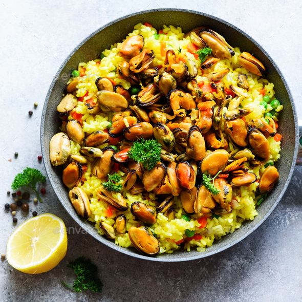Traditional spanish seafood paella in pan rice, peas, shrimps, mussels, squid on light grey concrete - Stock Photo - Images