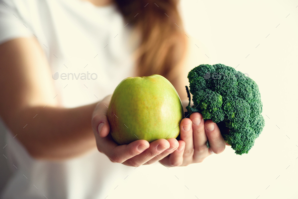 Woman in white T-shirt holding geen apple and broccoli in her hands. Copy space. Clean detox eating - Stock Photo - Images