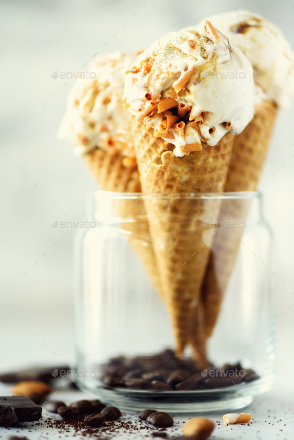 Caramel sauce ice cream in waffle cone with coffee beans on grey stone background. Summer food - Stock Photo - Images