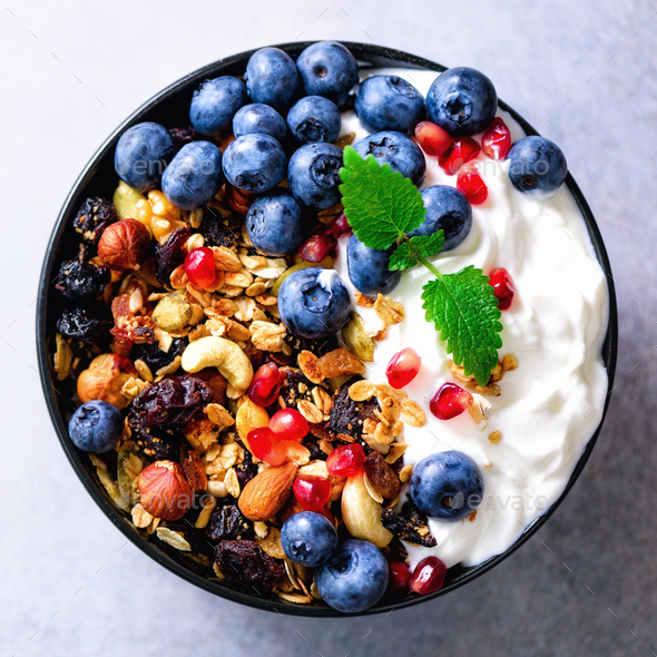 Tasty homemade granola, yogurt, fresh organic berries, pomegranate, mint on grey concrete background - Stock Photo - Images
