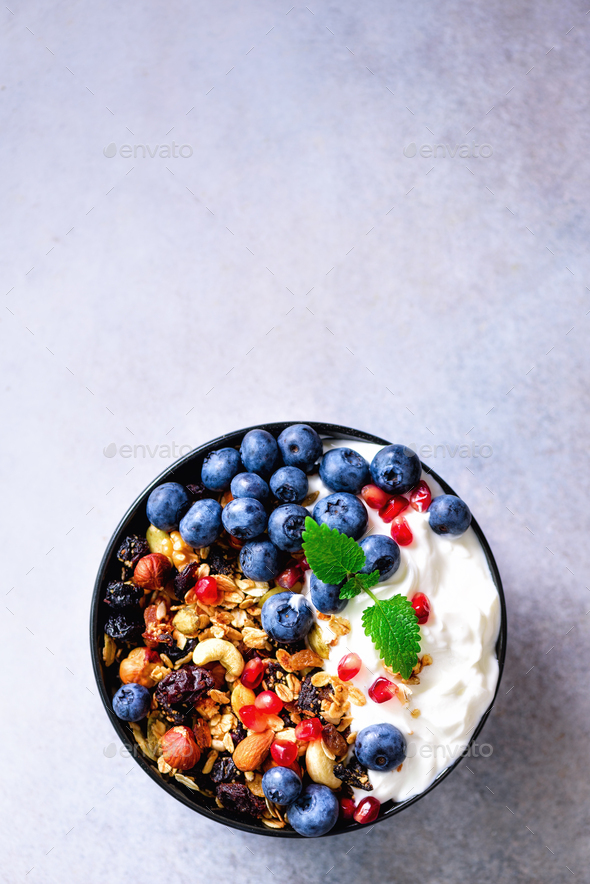 Tasty homemade granola, yogurt, fresh organic berries, pomegranate, mint on grey concrete background - Stock Photo - Images