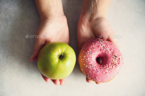 Young woman in white T-shirt choosing between green apple or junk food, donut. Healthy clean detox - Stock Photo - Images