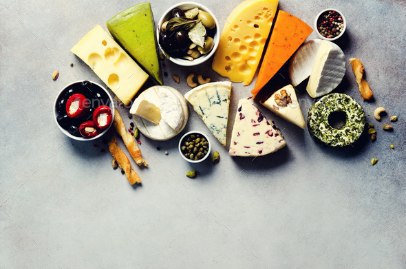 Assortment of hard, semi-soft and soft cheeses with olives, grissini bread sticks, capers, grape, on - Stock Photo - Images