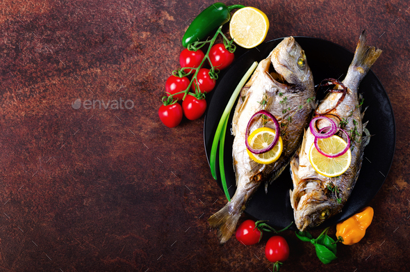 Cooked baked grilled fish, dorado, sea bream with lemon, herbs, vegetables and spices on rustic - Stock Photo - Images