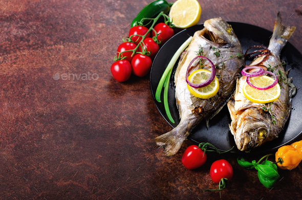Cooked baked grilled fish, dorado, sea bream with lemon, herbs, vegetables and spices on rustic - Stock Photo - Images