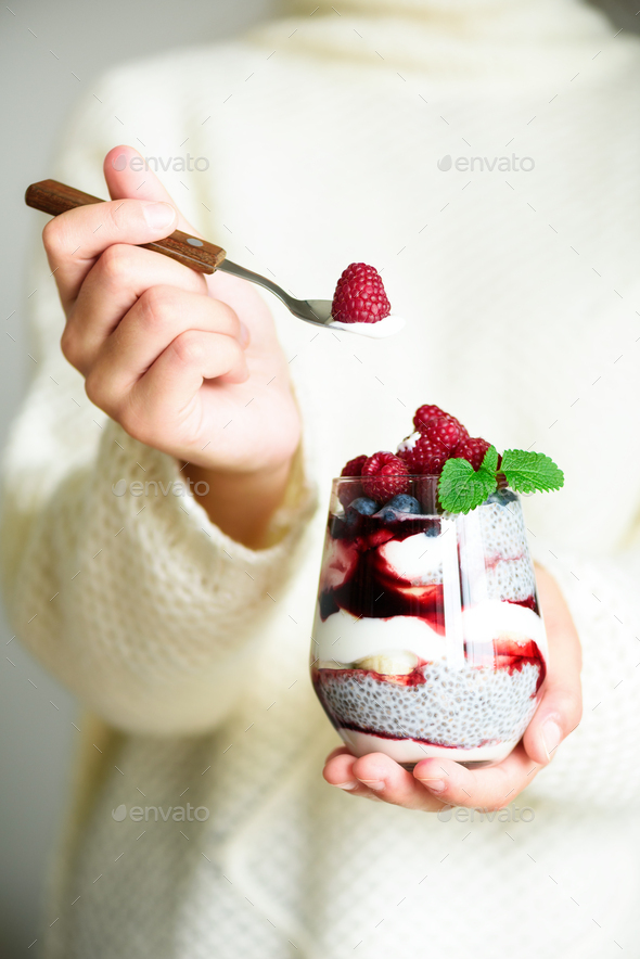 Girl in white sweater holds glass with chia milk dessert, raspberries, blueberries, mint. Healthy - Stock Photo - Images
